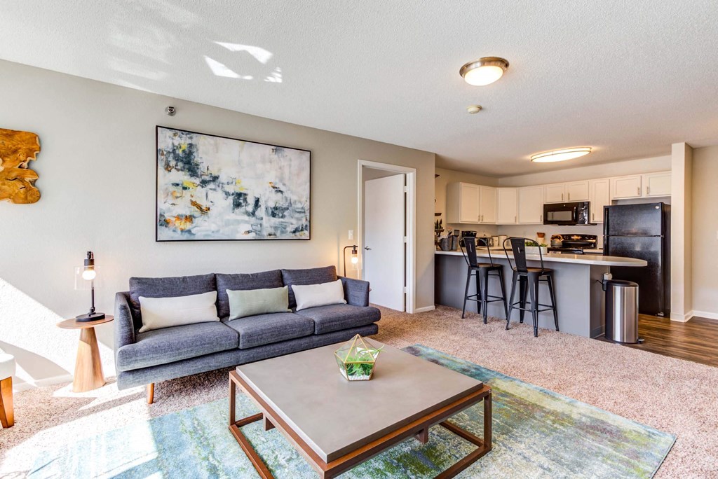 a living room with a couch coffee table and a kitchen in the background