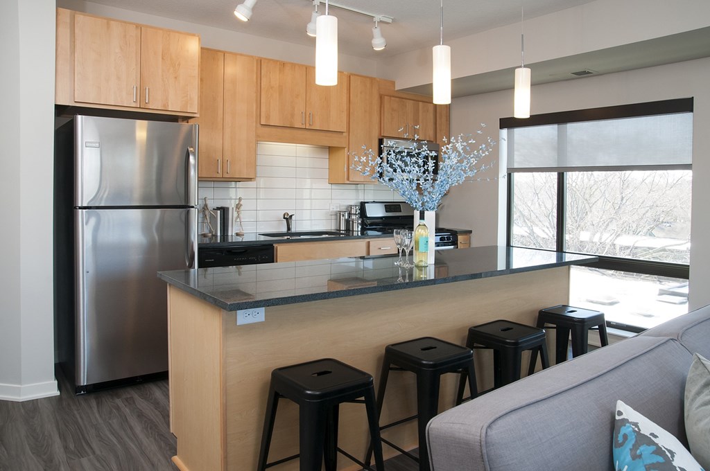 A kitchen with a refrigerator, stove, and bar stools.