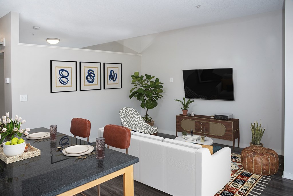 A modern living room with a white sofa, a black coffee table, and a TV on the wall.