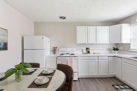 A kitchen with white appliances and cabinets, a dining table set with plates and a potted plant on it.
