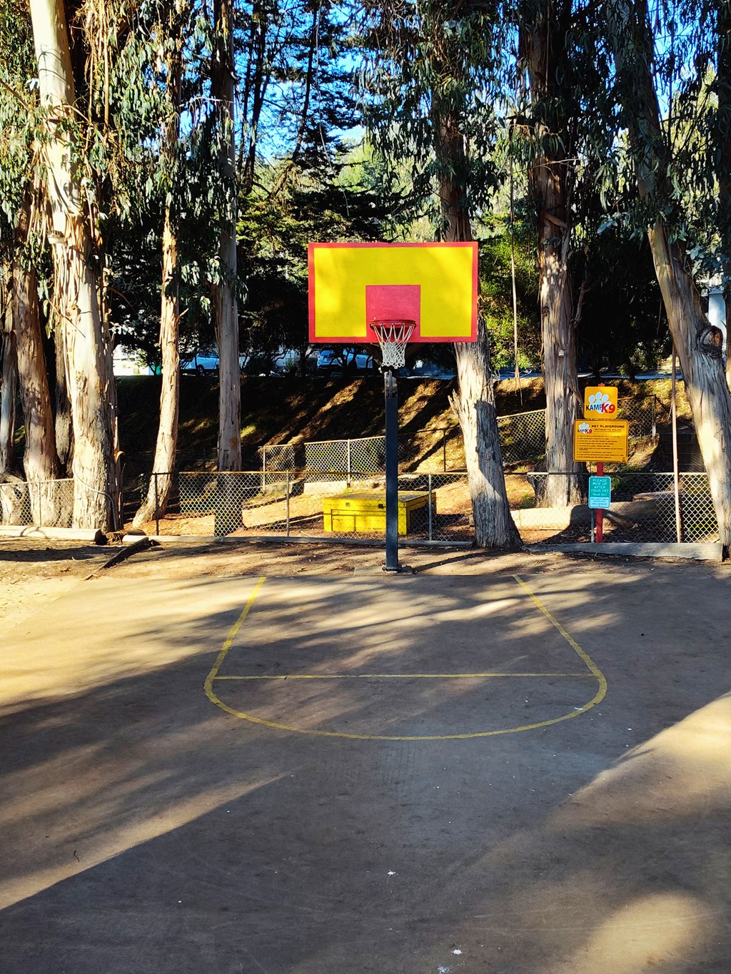 A basketball court surrounded by trees with a yellow hoop at Salinas Sunset Apartments, Salinas