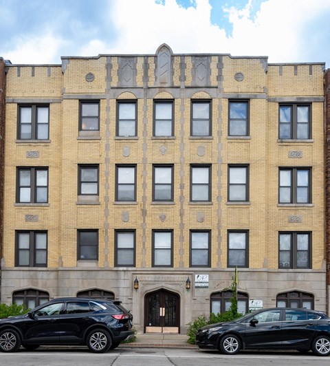Two black cars are parked in front of a tan building with a black door.
