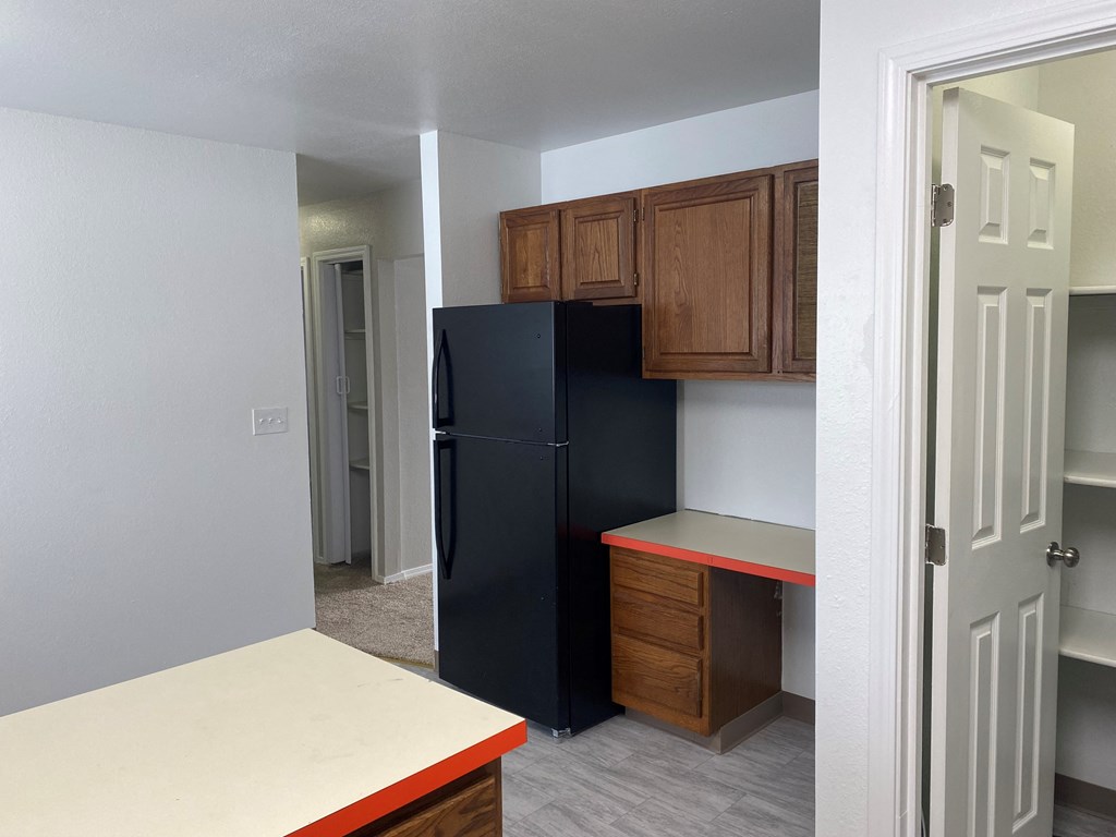 an empty kitchen with a black refrigerator and wooden cabinets