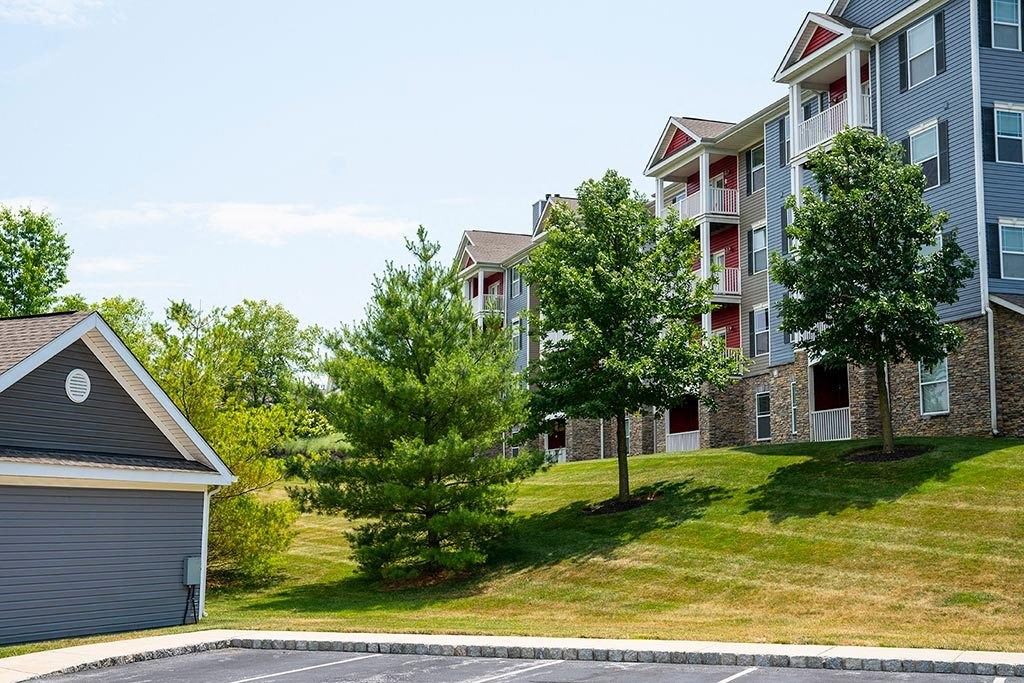 an apartment building on a grassy hill with trees  at ReNew Glenmoore, Pennsylvania, 19343