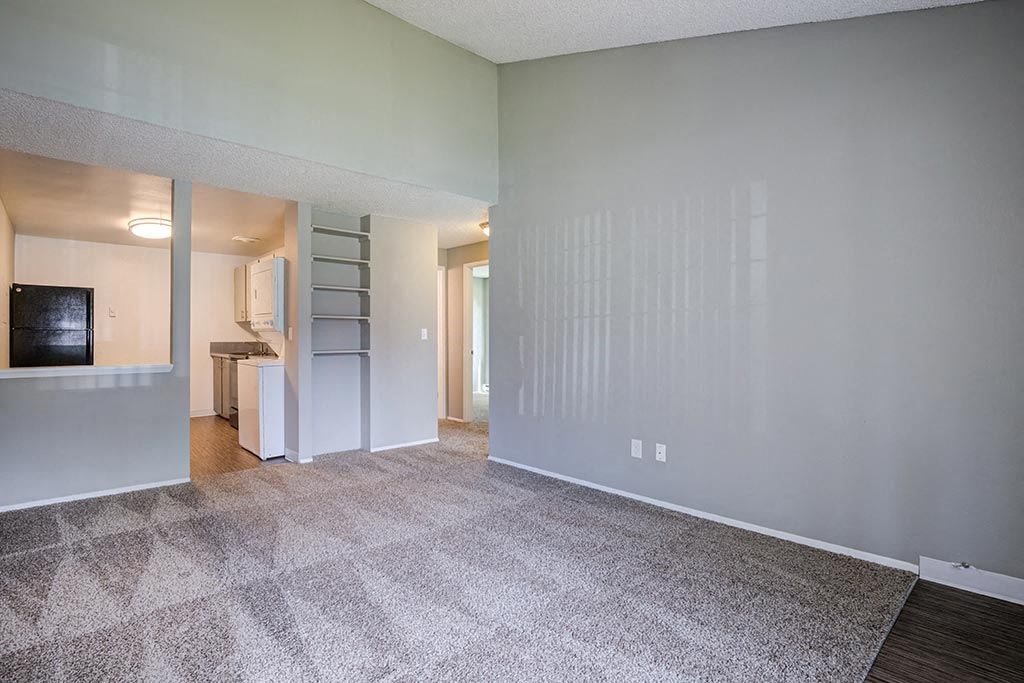 an empty living room with a kitchen in the background