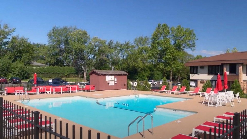 a swimming pool with red lounge chairs and a brown building in the background