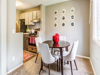 A dining room with a table and chairs and a red vase on the table.