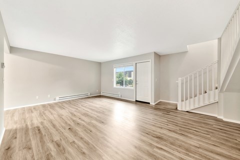 A spacious room with wooden flooring and a staircase on the right.