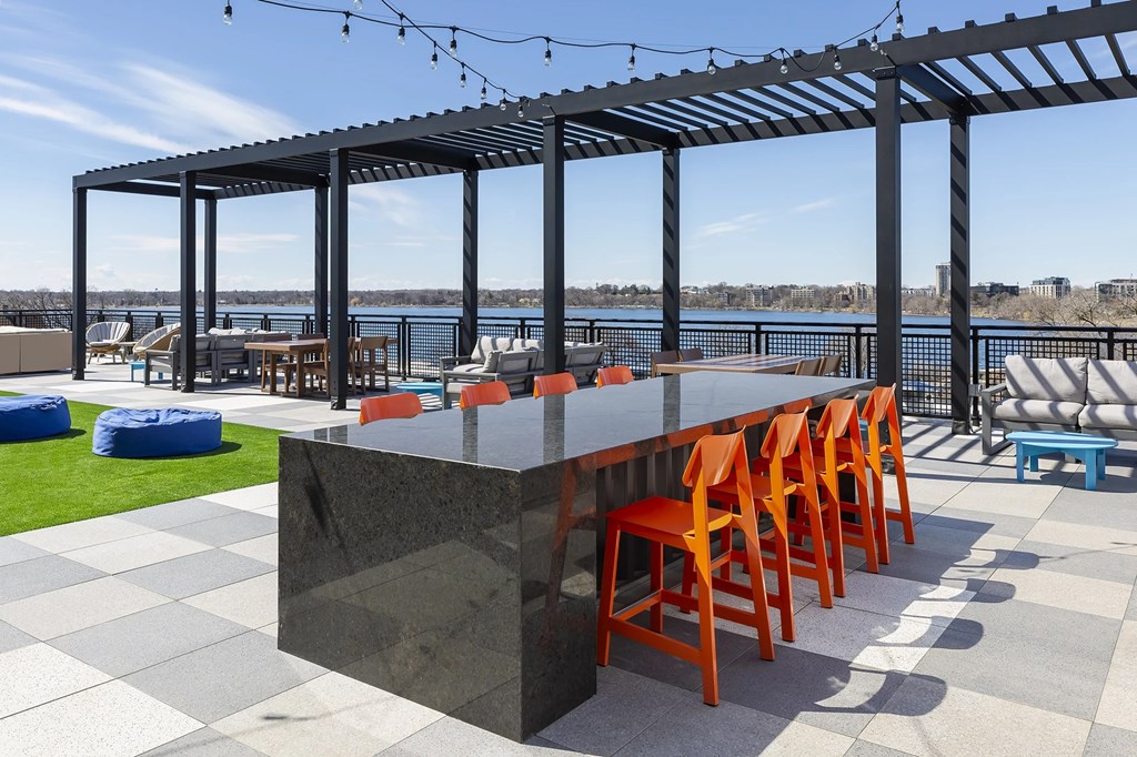 Bar with orange chairs and a black counter is set up on a patio with a view of the water.