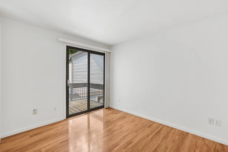 A room with wooden floors and a sliding glass door leading to a balcony.