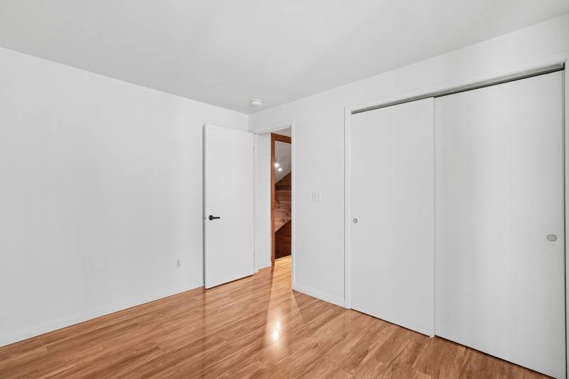 A room with white walls and wooden flooring with a white door on the left and a white closet on the right.