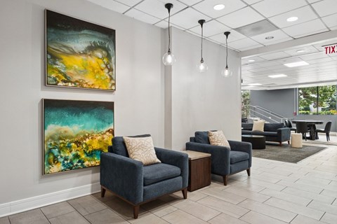 A living room with two blue couches and two paintings on the wall.
