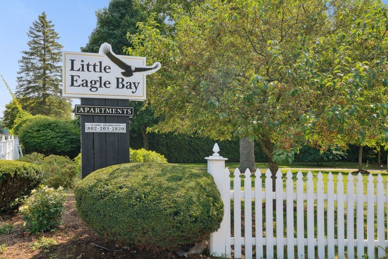 A sign for Little Eagle Bay Apartments stands in front of a white picket fence.