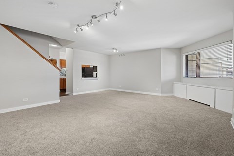 A spacious room with a carpeted floor and a staircase on the left side.