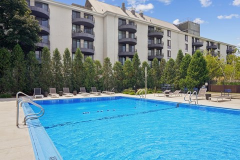 A swimming pool in front of a building with trees in the background.