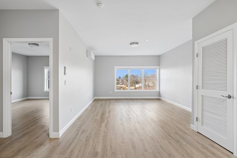 A room with wooden floors and a large window with a view of trees outside.