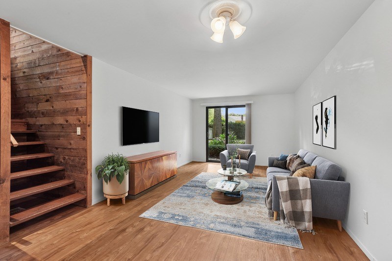 A living room with a grey couch, a wooden staircase, and a flat screen TV.
