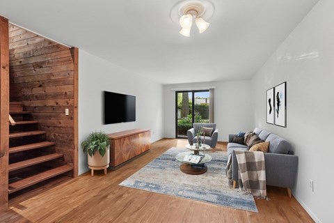 A living room with a grey couch, a wooden staircase, and a flat screen TV.