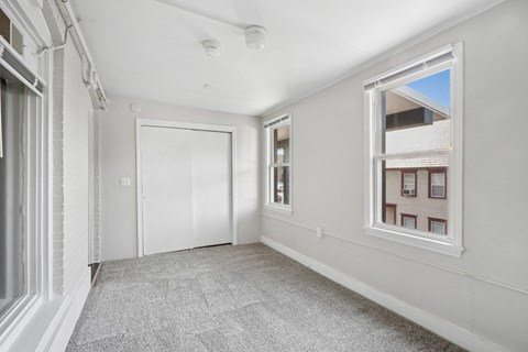 A room with a grey carpet and a window showing a building outside.