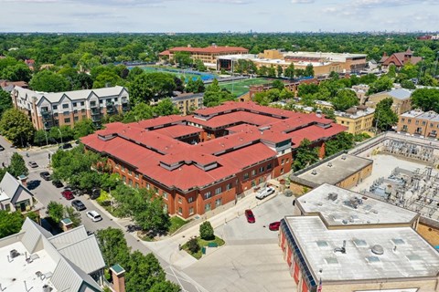 A large red building with a red roof is surrounded by trees and other buildings.