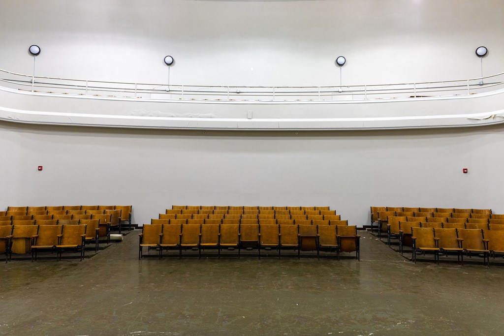 an empty auditorium with yellow seats and a white wall
