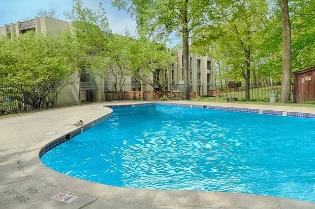 A swimming pool surrounded by trees and an apartment building in the background at Wayzata Woods Apartments, Minnesota, 55391