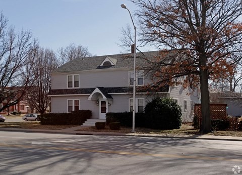 A house with a grey roof and a white door is surrounded by trees and bushes.