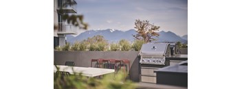 A barbecue grill is on a patio with a table and chairs.