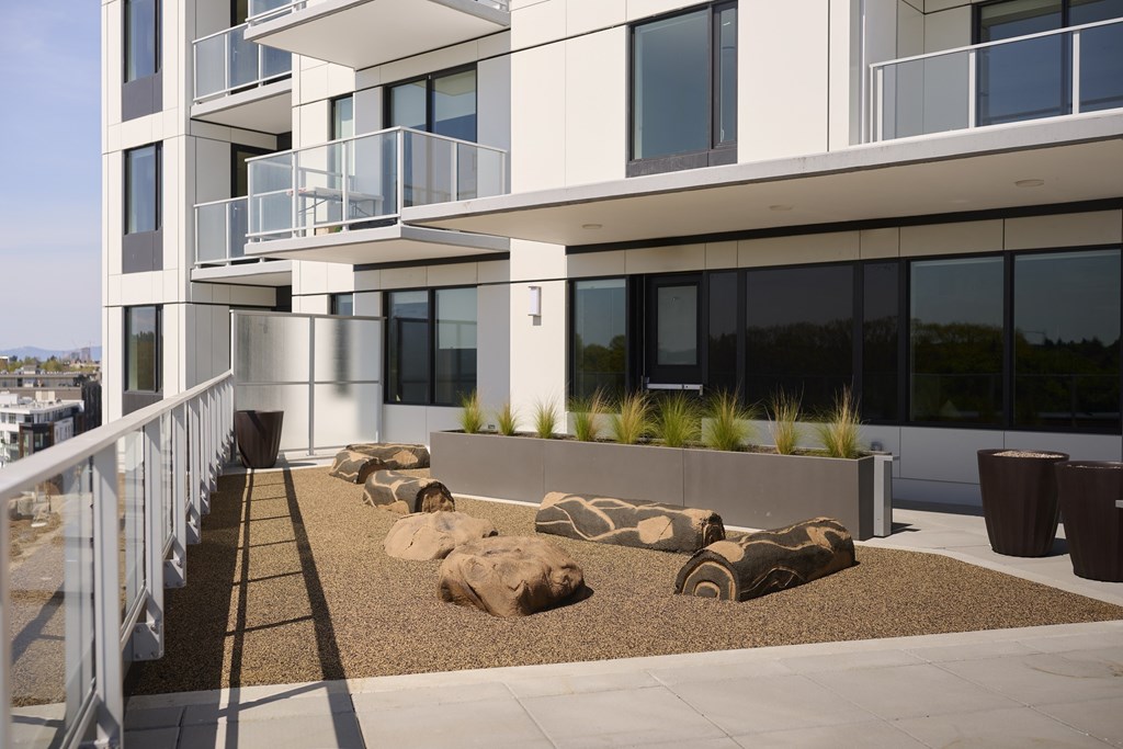 A modern building with a balcony and a landscaped area in front.