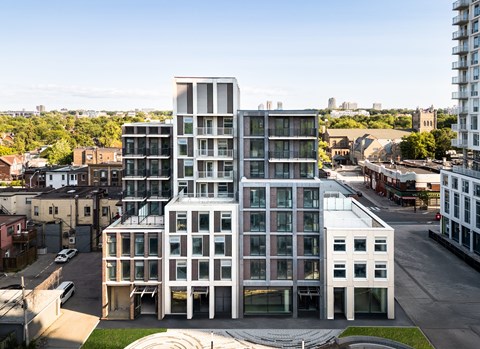 A modern building with a glass facade is surrounded by other buildings and greenery.
