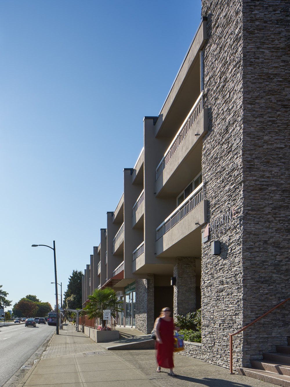 A woman in a red dress is walking down a sidewalk next to a stone building.