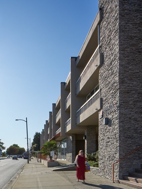 A woman in a red dress is walking down a sidewalk next to a stone building.