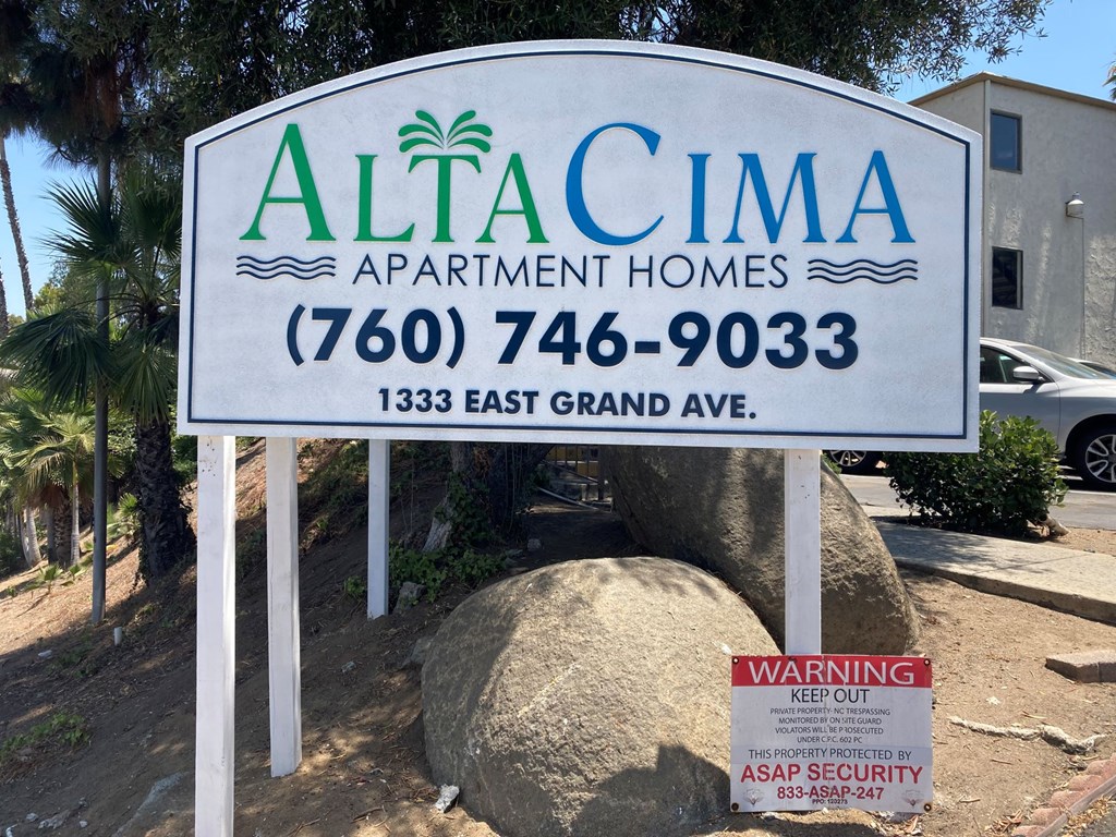 A sign for AltaCima Apartment Homes with a warning sign below it.