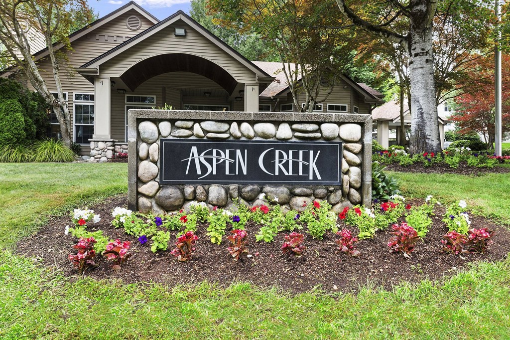 A stone sign that says Aspen Creek in front of a house.