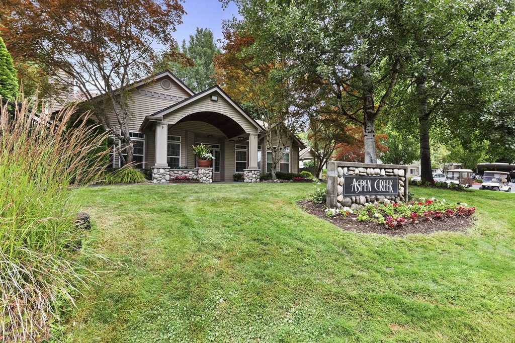A small house with a porch and a sign that says "Aspen Creek" in front of it.