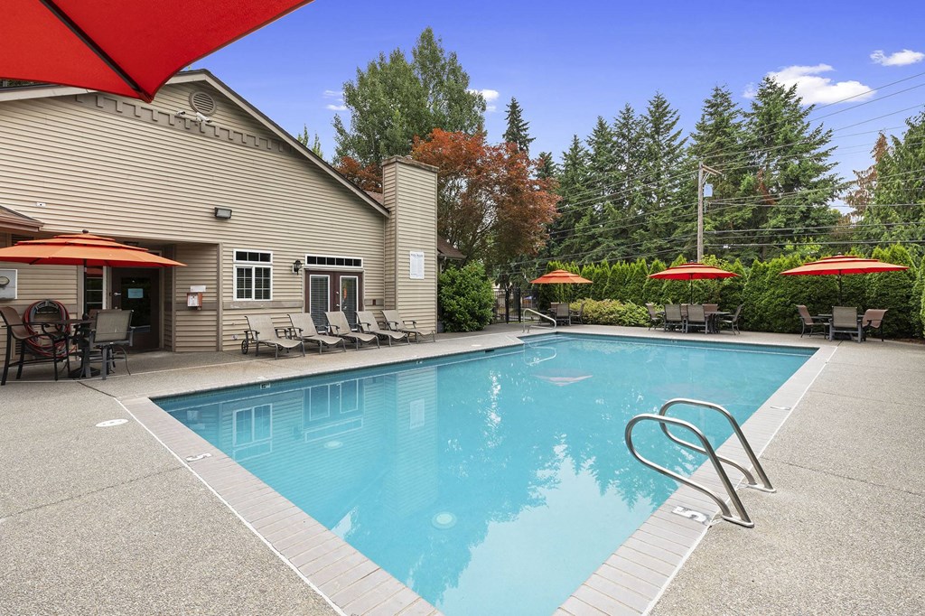A swimming pool with a diving board and red umbrellas.