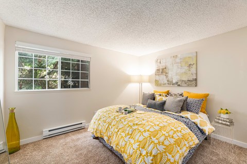 A bedroom with a yellow bedspread and a window with blinds.