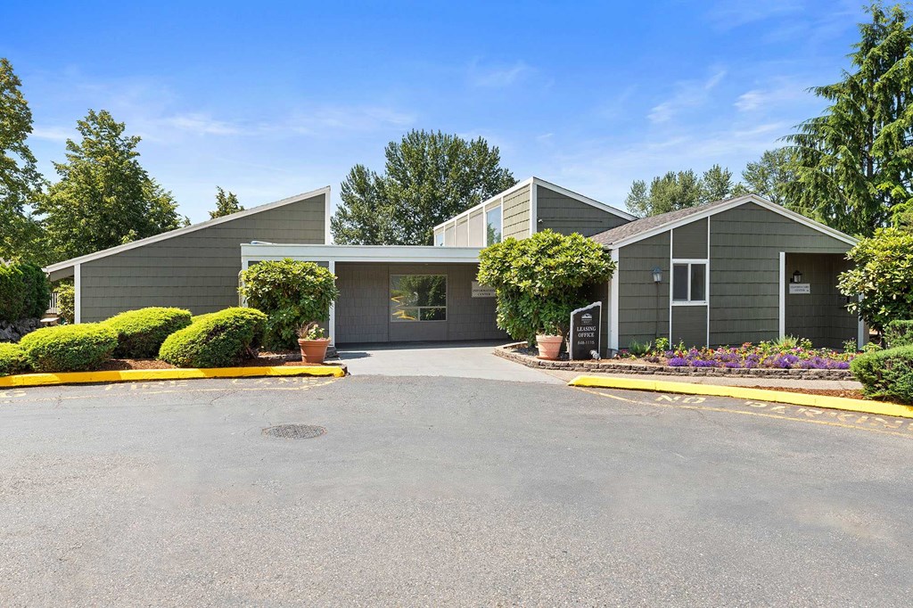 A parking lot in front of a building with grey walls and a white roof.