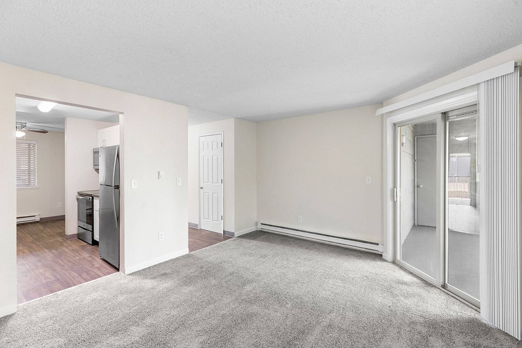 A spacious living room with a grey carpet and a white door.