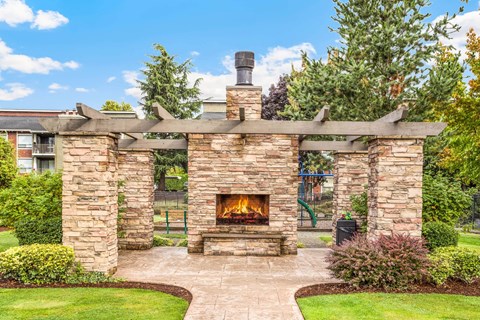 A stone fireplace is the centerpiece of a landscaped yard.