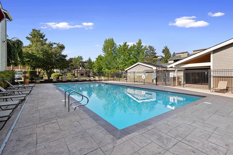 A swimming pool surrounded by a tiled patio and lounge chairs.