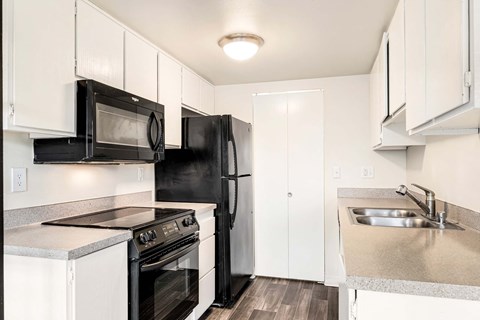 A black refrigerator sits in a kitchen with white cabinets and a stainless steel sink.