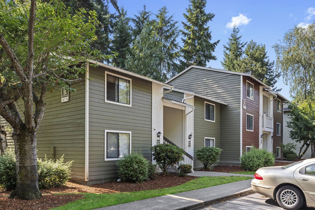 A car is parked on the street in front of a two-story apartment building.