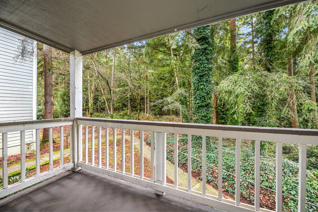 A white railing on a porch leads to a wooded area.