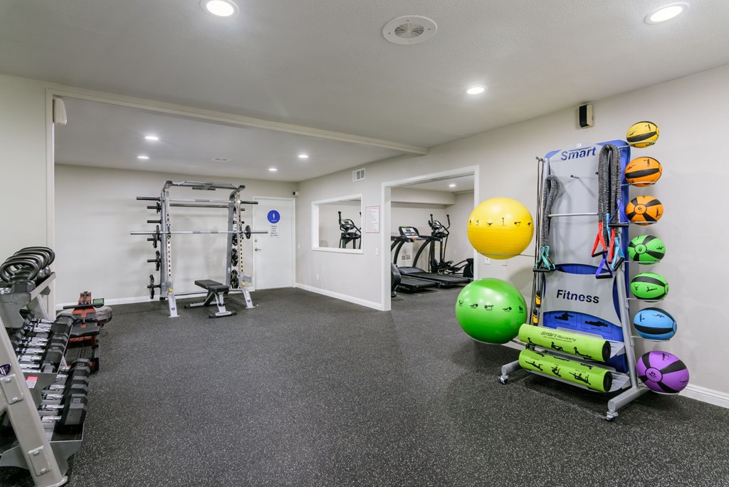 A fitness room with a variety of equipment including a weight rack, exercise balls, and a treadmill.
