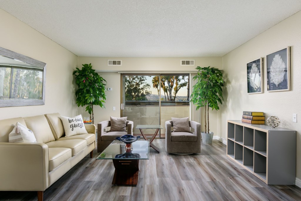 A living room with a tan couch, a glass table, and a large window.