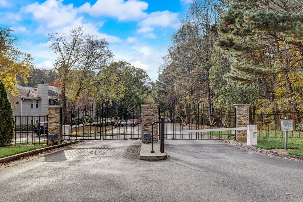 the gate at the end of a driveway with a house behind it