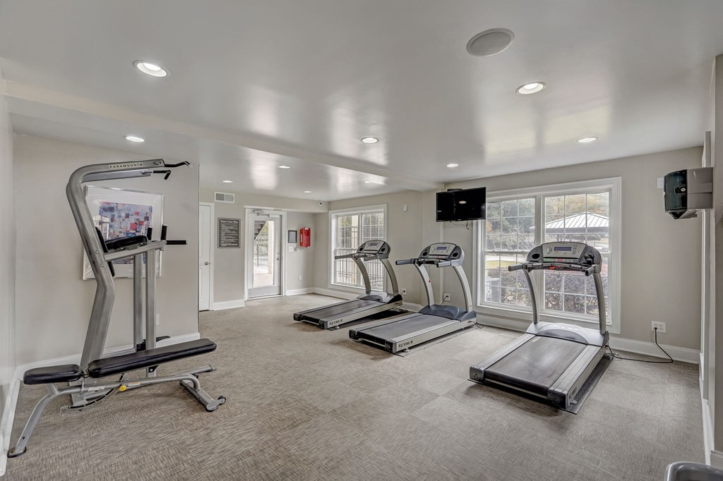 a gym with treadmills and other exercise equipment in a room with windows and white walls