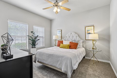 A bedroom with a bed, a ceiling fan, and a nightstand with a lamp.