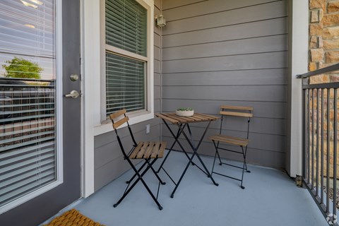 A small table and two chairs are on a porch.